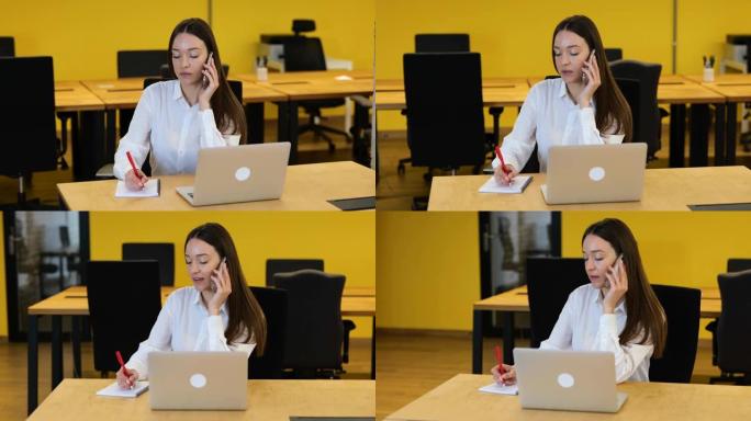 慢动作视频。白人妇女坐在现代办公室的工作桌面上，通过电话交谈并在笔记本上写下。