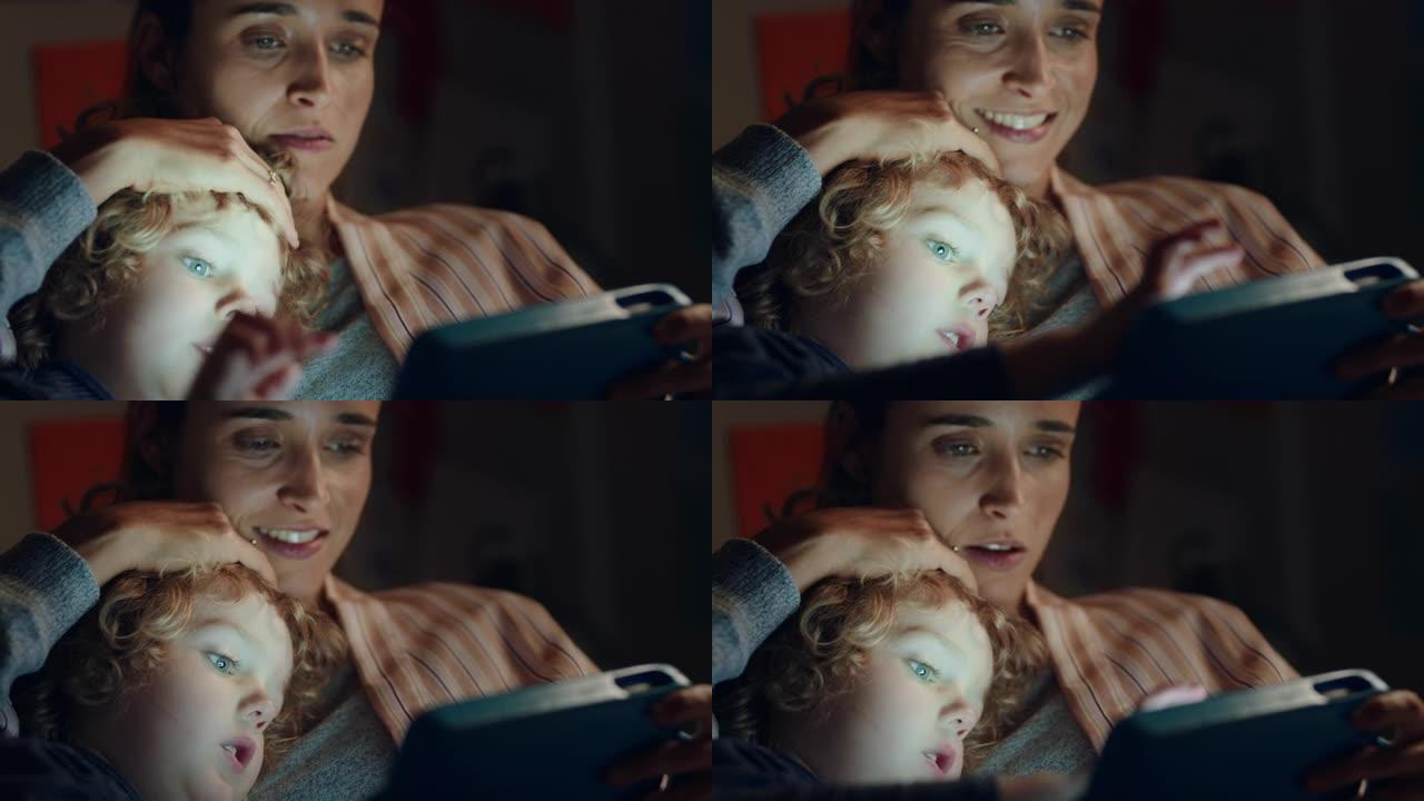 快乐的小男孩使用平板电脑，母亲教孩子在触摸屏技术上玩游戏睡前玩得开心