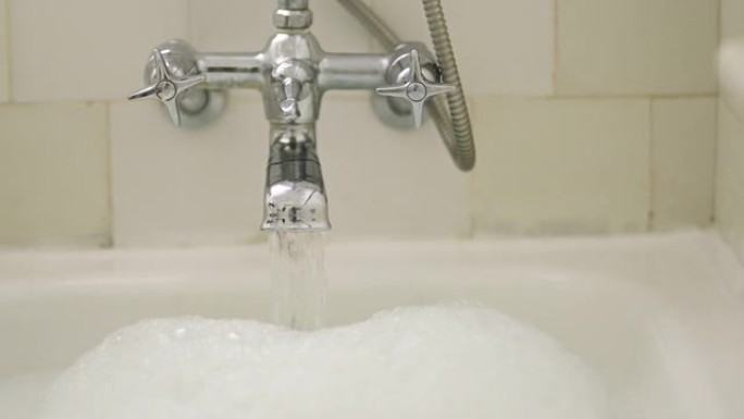 水龙头、流动水和浴室的泡泡浴清洁、放松和洗涤，以实现自我护理和禅。家用镀铬水龙头，浴缸中有液体流动，