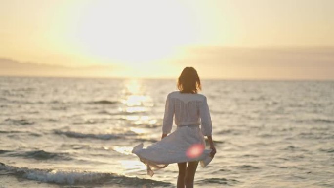 无忧无虑的女人的轮廓，张开双臂站在海滩上，在海洋上享受橙色的日落。日落时的女孩剪影。