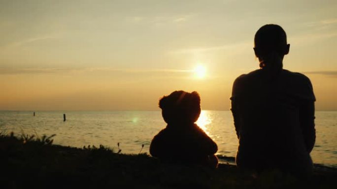 湖上一个女人和一只泰迪熊的轮廓，在太阳落山的地平线上向前看