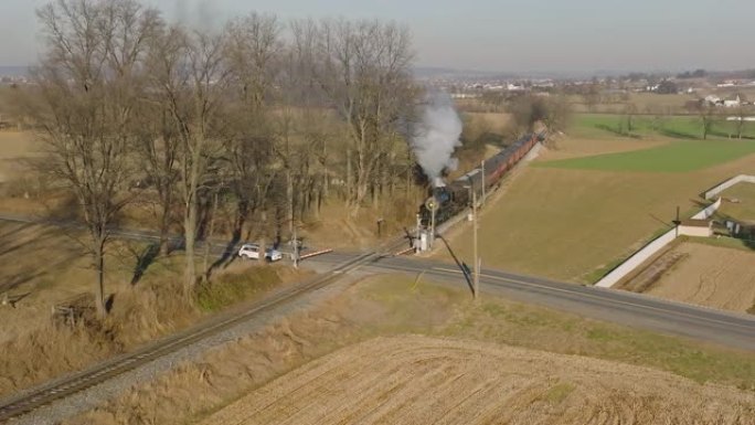 无人机以慢动作缩小正在接近的蒸汽旅客列车，正在接近十字路口的视图