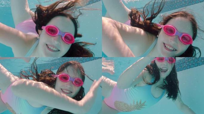 快乐的女孩在游泳池水下游泳微笑挥手享受在水晶般清澈的水中游泳戴着护目镜享受夏天4k