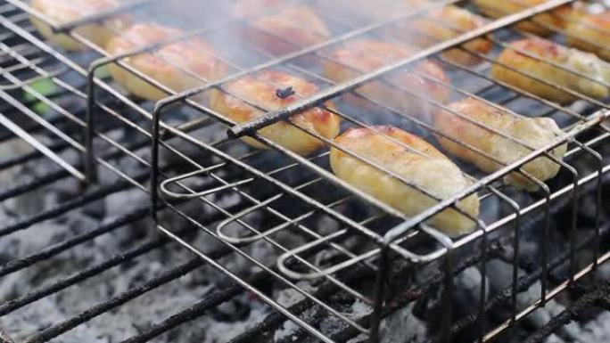 多汁的烧烤香肠香肠在烤架上褐变，在闷烧的煤特写镜头上燃烧着火焰和烟雾。在户外烤架上烧烤香肠 -- 在