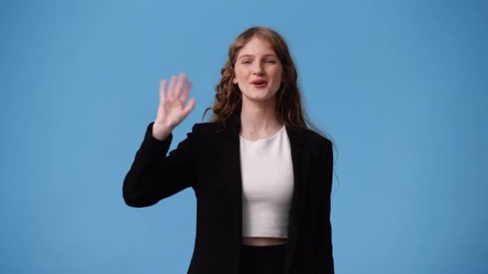 可爱的女孩在蓝色背景上挥手打招呼的4k视频。