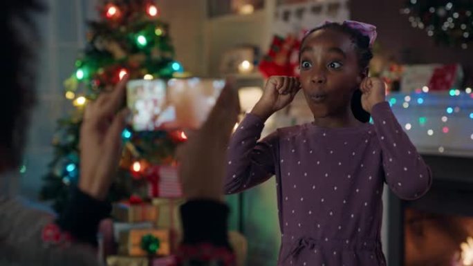圣诞有趣的非洲裔美国女孩给妈妈做鬼脸用智能手机拍照在家里享受节日记忆4k