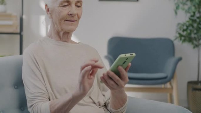 快乐的老年女士慢动作肖像使用智能手机触摸屏在家室内享受内容
