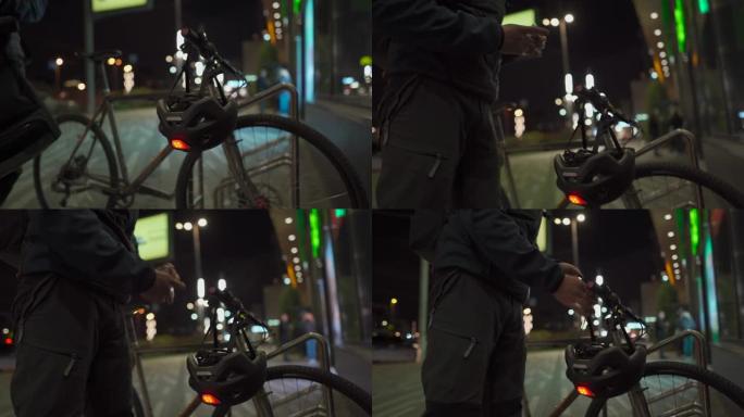 戴着医用口罩的骑自行车的人从商店出来，步行到停放的自行车用消毒剂治疗他的手，晚上在城市戴上带有红色闪