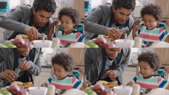 快乐的小男孩早餐吃新鲜华夫饼，父亲倒蜂蜜，在家厨房为儿子准备美味的自制食物4k