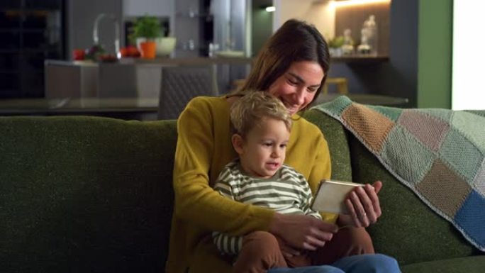 小家庭使用智能手机与远亲进行视频通话，而坐在家里穿着睡衣。快乐的年轻母亲和她的儿子使用互联网与朋友交
