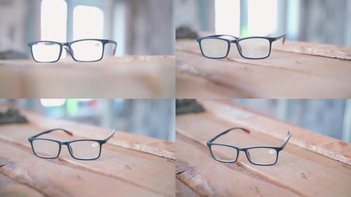 黑框大凸透镜眼镜在建筑工地模糊背景上的木板上特写镜头，平滑的相机移动。房间维修的准确性，工作时划伤的