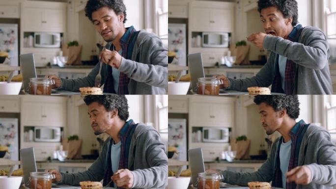 快乐的混血男子使用笔记本电脑在厨房工作吃华夫饼早餐在线浏览在家享受放松的早晨