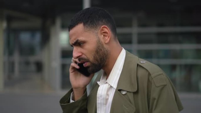 一位阿拉伯绅士在市区外的蜂窝设备上交谈，表情严肃。集中的中东男性个人将手机抓在耳朵里