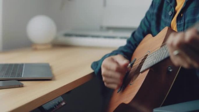 亚洲人在家练习弹吉他，使用笔记本电脑观看大师班提高技能。