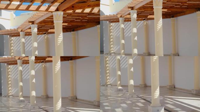 凉亭的木结构由遮蔽凉亭的光滑圆柱形白色圆柱支撑，屋顶被玻璃覆盖，与砖砌屋顶的挡土墙相连