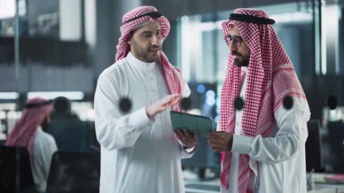 两个多民族的阿拉伯同事在忙于软件开发项目时进行了交谈。工程师与中东项目经理交谈，在办公室使用平板电脑