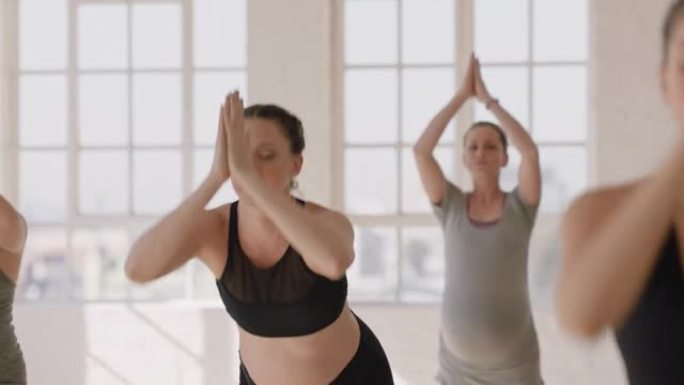 年轻的怀孕白人妇女在瑜伽课上练习站立向前弯曲姿势享受健康的生活方式团体在健身工作室锻炼