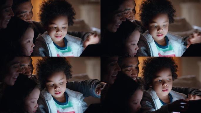 幸福的家庭使用平板电脑，带孩子母亲和父亲看着孩子在触摸屏技术上玩游戏，享受睡前放松的夜晚