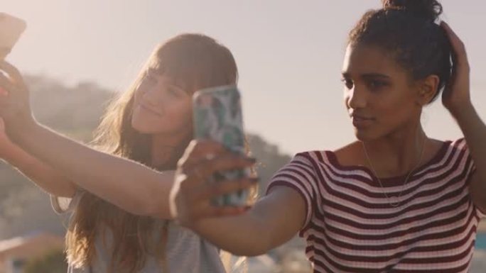 美丽的年轻女性朋友使用智能手机自拍，享受日落时在屋顶上闲逛，准备周末派对