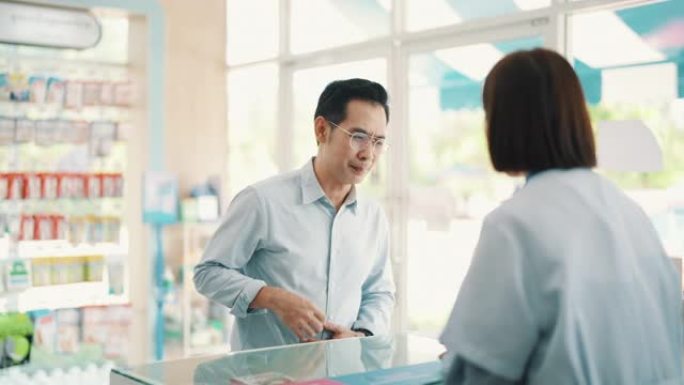 客户从药房的药剂师那里获得帮助。亚洲女药剂师帮助成熟的男性顾客提供药物推荐。小企业。药。健康概念