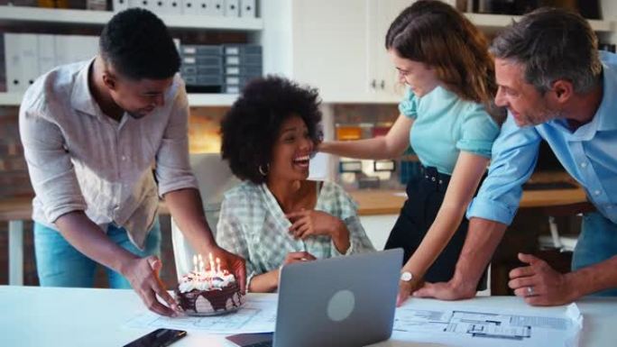 员工在建筑师办公室庆祝女同事的生日，并以慢动作拍摄惊喜蛋糕