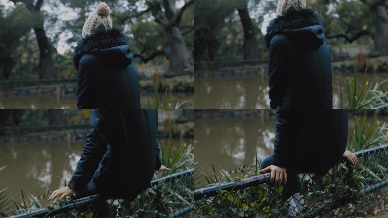 年轻女子独自坐在公园里享受宁静的自然池塘孤独的少女在寒冷的阴天感到沮丧