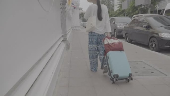 享受曼谷旅游目的地亚洲女性旅游地标的旅行者。泰国曼谷，一名女游客拖着行李箱在寺庙墙Wat Phra 