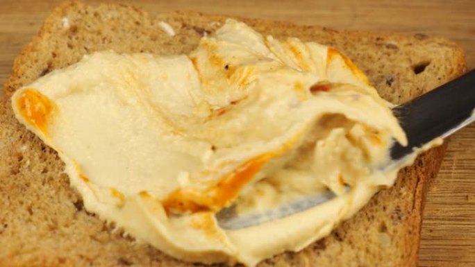 鹰嘴豆泥用刀子铺在一块木菜板上的杂粮面包上。素食主义者的食物。