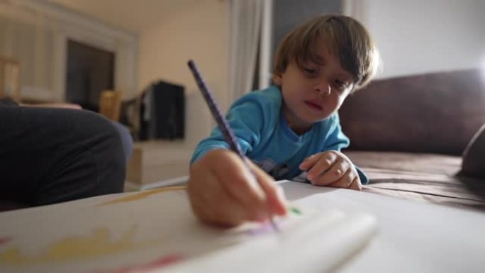 一个小男孩用彩色铅笔在纸上涂鸦。关闭笔记本上的儿童手着色。儿童发展活动