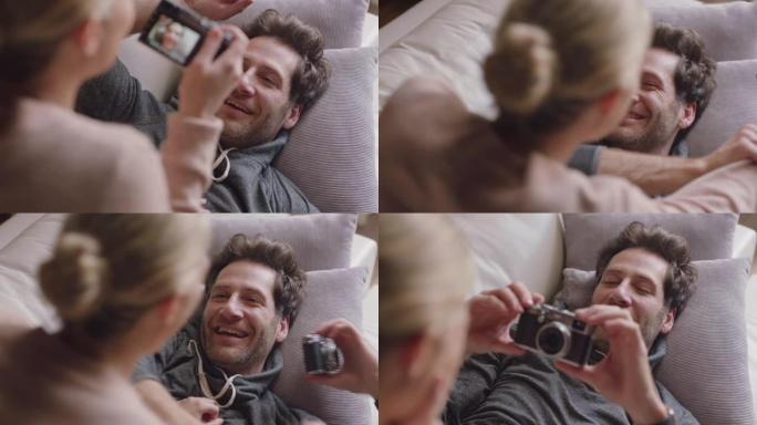 快乐的年轻夫妇一起用相机拍照在沙发上玩得开心，享受浪漫的关系，互相拍脸