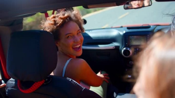在公路旅行中，笑的女性朋友在敞开车中玩耍的肖像
