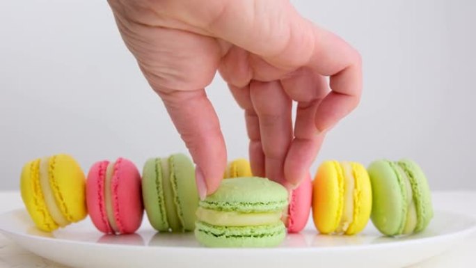 许多彩色的法国马卡龙甜点站在白色背景上的盘子上，一只手在一个圆圈中扭曲了一个绿色，为咖啡店做广告。