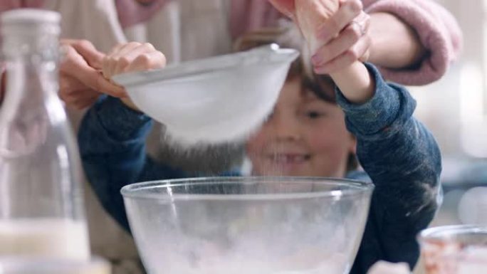 小男孩帮助母亲在厨房里烘烤混合配料用筛子筛分面粉在家准备纸杯蛋糕的配方