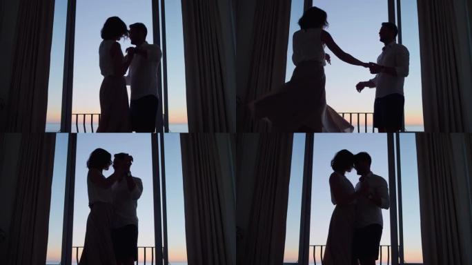 剪影快乐的夫妇在日落时在酒店房间跳舞，享受蜜月假期，享受美丽的海景庆祝假期