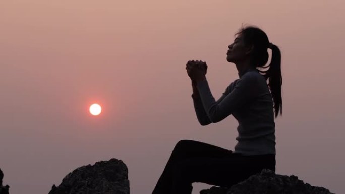 女人在美丽的日出背景上祈祷的剪影，视频4k慢动作。