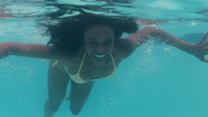 美丽的非洲裔美国妇女在游泳池水下游泳微笑漂浮在蓝色水晶清澈的水中玩得开心在夏季4k