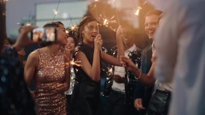 快乐的时尚朋友在迷人的屋顶派对上跳舞庆祝新年前夜，朋友使用智能手机在社交媒体4k上分享庆祝视频