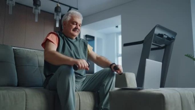退休男子在家训练以节省健康和保持健康，通过笔记本电脑观看在线锻炼