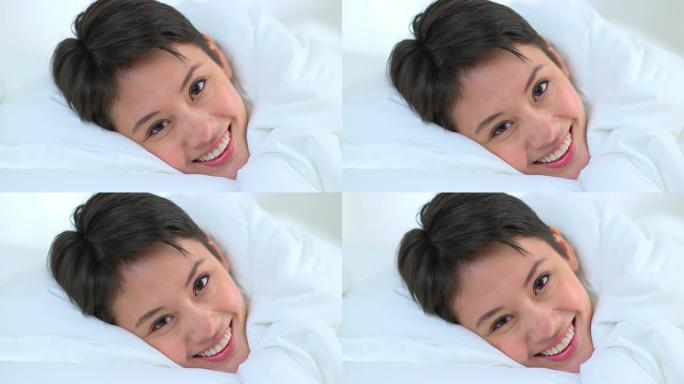 特写镜头多莉，亚洲女人在床上的床单下微笑