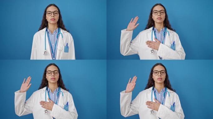 年轻美丽的西班牙裔女医生用手在孤立的蓝色背景上发誓