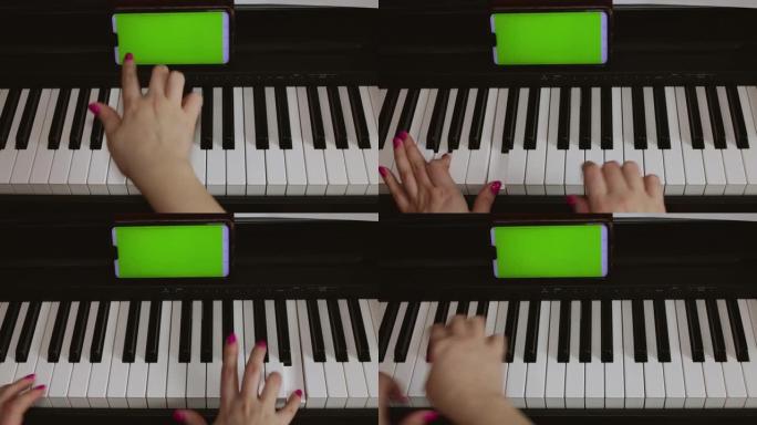 一个女人从手机上记录的音符学习弹钢琴。钢琴，女性手和带有绿色屏幕的电话的特写镜头