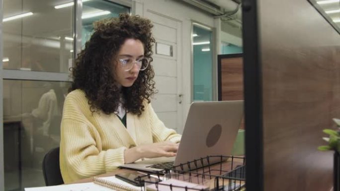 女自由职业者在同事办公室的小隔间里在笔记本电脑上打字
