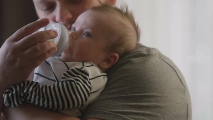 爸爸穿着紧身衣用奶瓶喂养新生婴儿