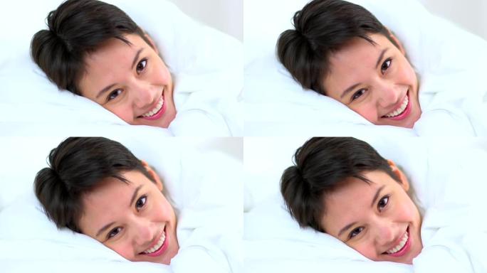 特写镜头多莉，亚洲女人在床上的床单下微笑