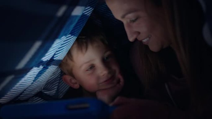 快乐的母子俩在毯子下使用平板电脑小男孩在触摸屏技术上玩游戏，妈妈睡前放松娱乐