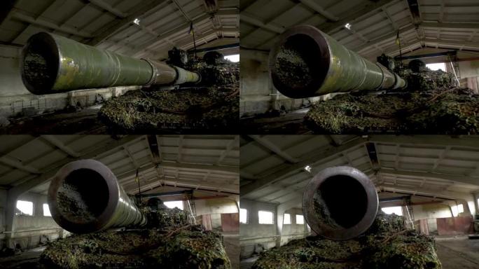坦克枪口的特写慢慢转向侧面。伪装网机库里的坦克。战争