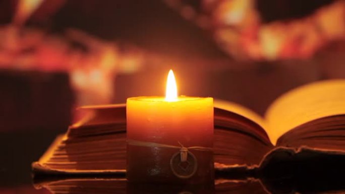 在火的背景下打开的书中的蜡烛。滑块镜头。