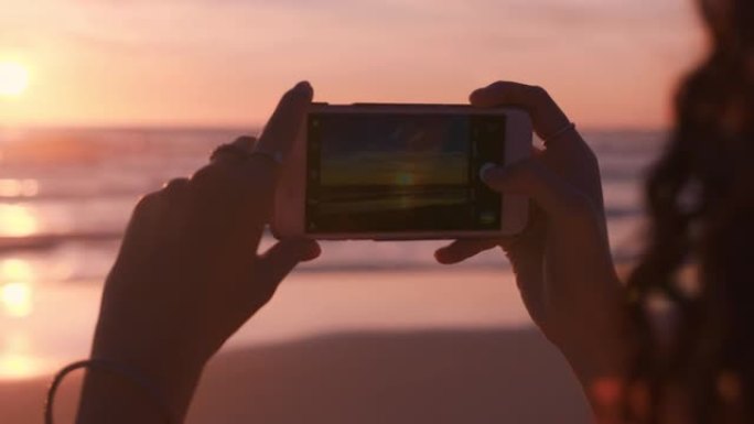 关闭海滩上的年轻女子使用智能手机拍摄美丽的日落享受分享暑假旅游经验在社交meda