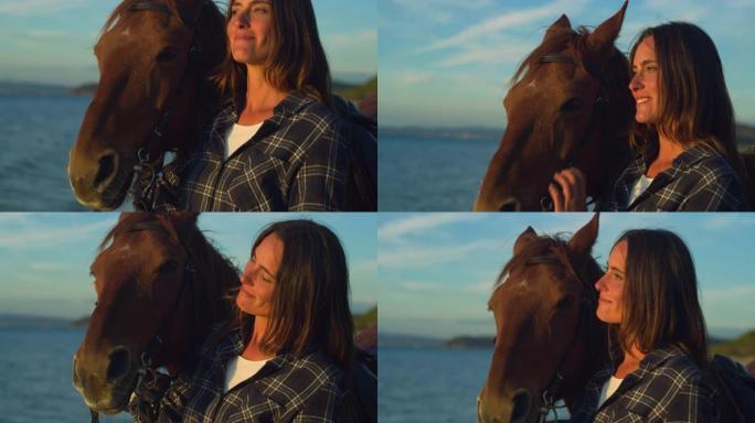 日落时，一个幸福美丽的女人和她的马在海边海滩上的特写肖像。职业女马术在看海时拥抱爱抚纯种马