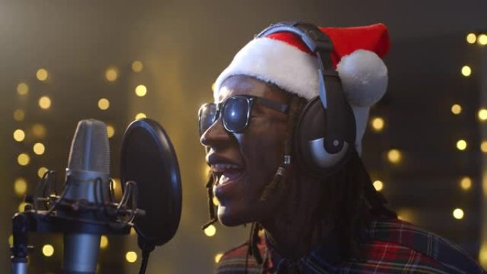 一位职业男性黑人歌手的特写肖像在录音室为他的圣诞节专辑录制了一首歌。非洲年轻艺术家戴着圣诞老人的帽子
